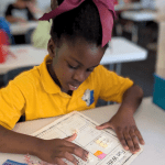 A young Lakeside Christian School elementary student wearing her uniform polo shirt works on a math assignment at her classroom desk, focused and engaged in learning.