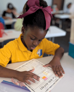 A young Lakeside Christian School elementary student wearing her uniform polo shirt works on a math assignment at her classroom desk, focused and engaged in learning.